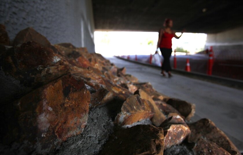 A woman walks past riprap that the city recently installed on Imperial Avenue below an Interstate 5 overpass to deter homeless encampments on the street.