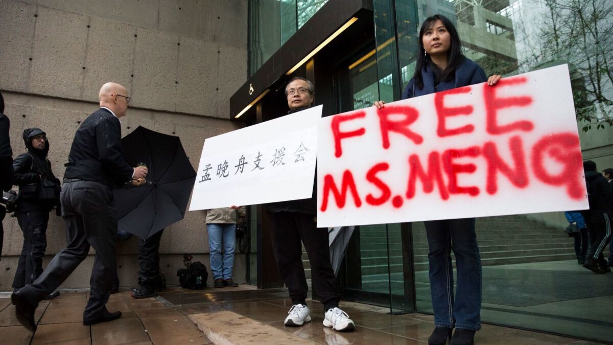 Ada Yu, right, and Robert Long hold signs in support of Huawei Technologies Chief Financial Officer Meng Wanzhou outside the courthouse in Vancouver, Canada, during her bail hearing Tuesday.