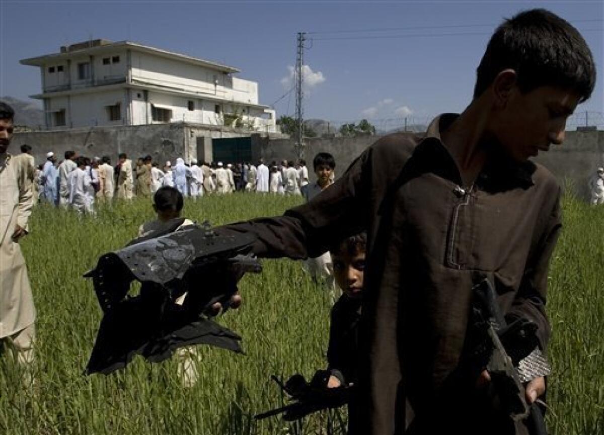 A Pakistani youngster shows metal pieces collected from wheat field outside a house, seen background, where al-Qaida leader Osama bin Laden lived in Abbottabad, Pakistan, on Tuesday, May 3, 2011. Local residents showed off small parts of what appeared to be a U.S. helicopter that Washington said malfunctioned and was disabled by the American commando strike team as they retreated, while Pakistan's leader on Tuesday denied suggestions that his country's security forces had sheltered Osama bin Laden. (AP Photo/Anjum Naveed)