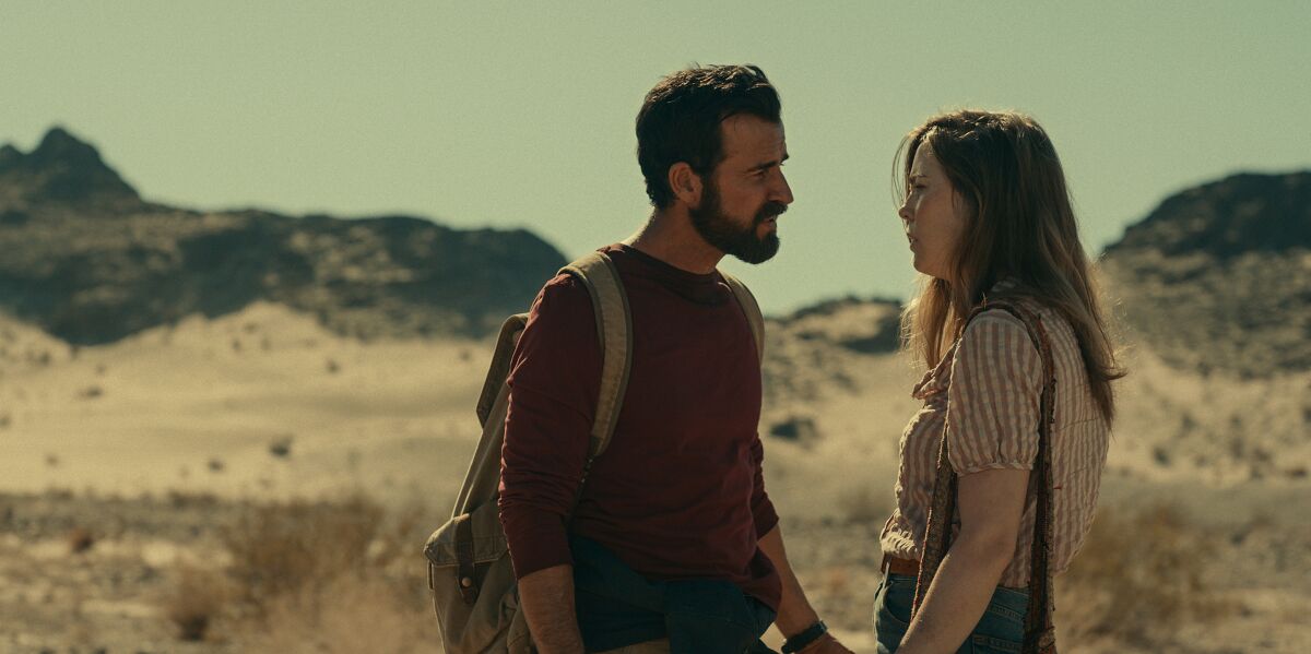 Justin Theroux, with a backpack, and Melissa George stand facing each other in the desert.
