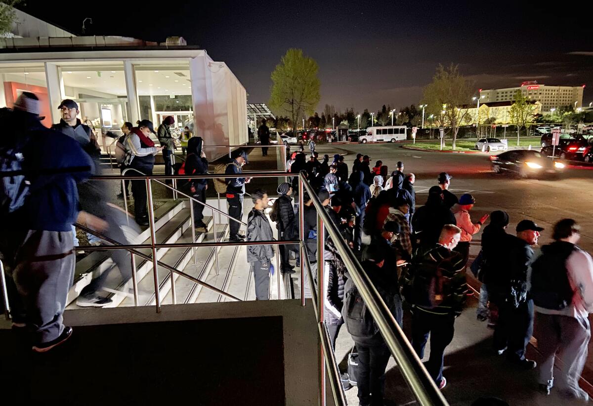 Tesla workers coming off the night shift wait to board buses outside the Fremont factory