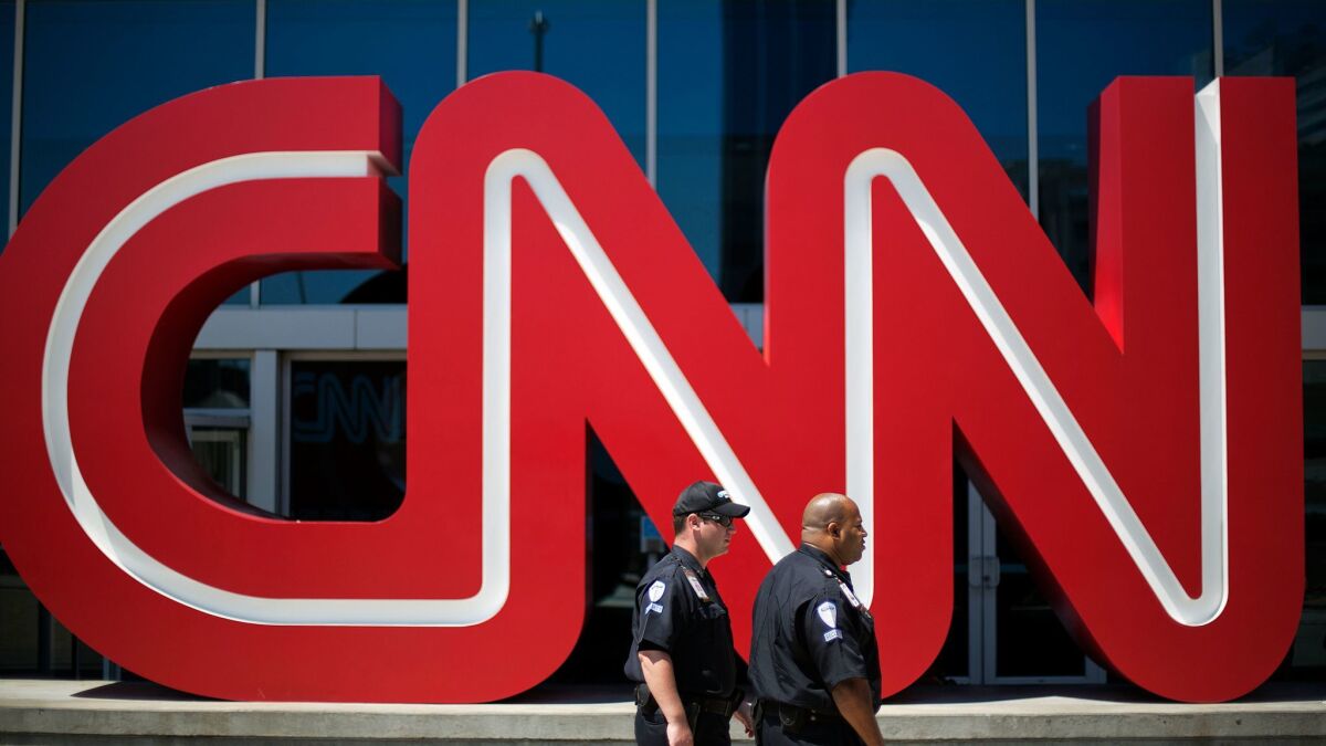 Security guards walk past the entrance to CNN headquarters in Atlanta. CNN is owned by Time Warner Inc., which is pursuing a sale to AT&T.