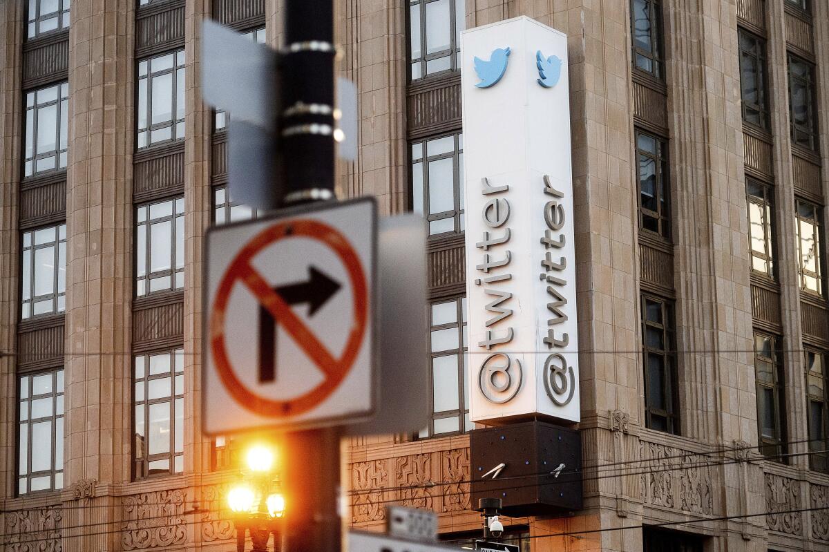 A sign with the Twitter name and bird logo hangs from a building.