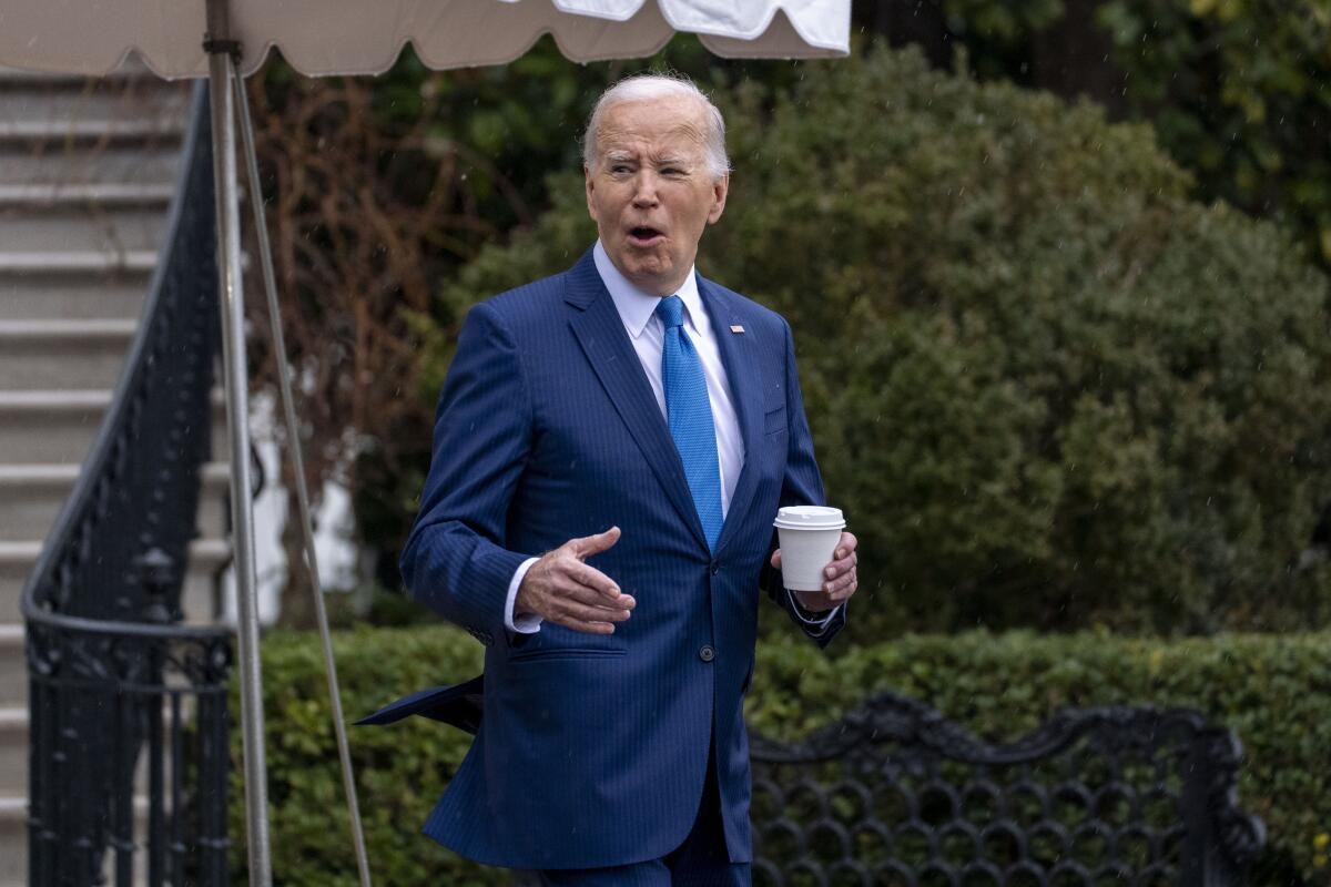 President Biden walks out of the White House holding a cup of coffee.