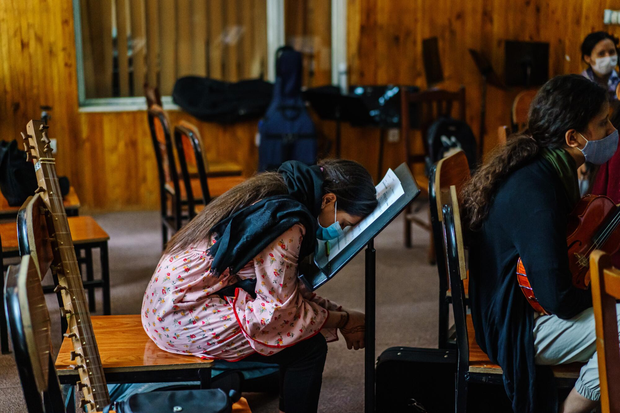 An Afghan girl in a loose pink, floral tunic rests her head on a music stand during class