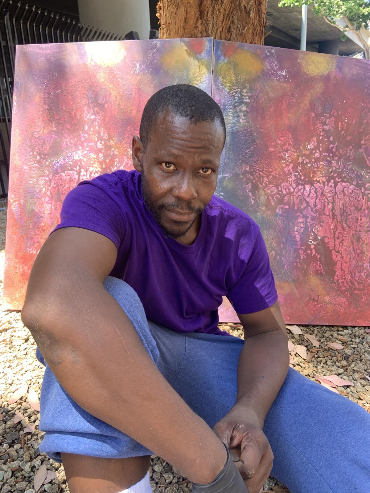 A Black man sitting outside with a painting behind him