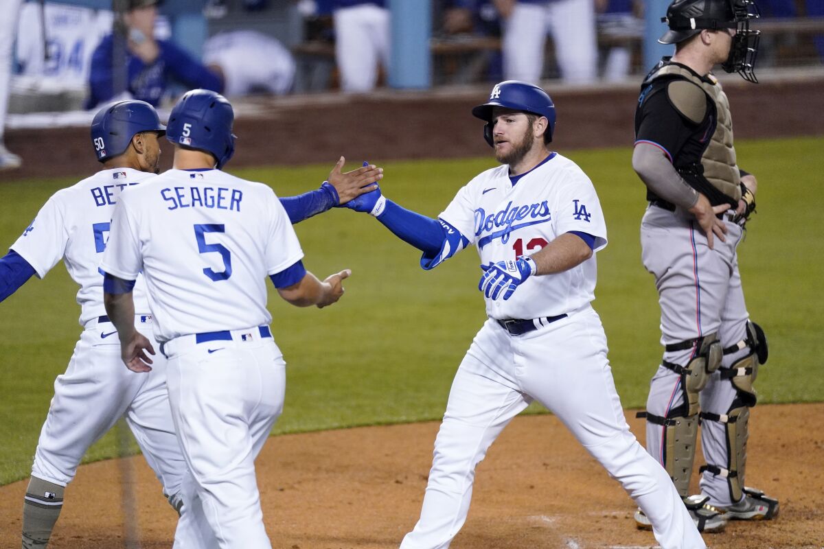 Los Angeles Dodgers' Max Muncy, second from right, is congratulated by Mookie Betts, left, and Corey Seager, second from left, after hitting a three-run home run as Miami Marlins catcher Chad Wallach stands at the plate during the second inning of a baseball game Friday, May 14, 2021, in Los Angeles. (AP Photo/Mark J. Terrill)