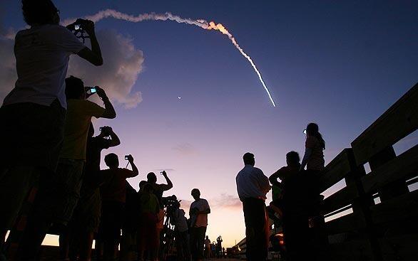 People at Jetty Park snap pictures of a Delta 2 rocket as it streaks by a crescent moon from Cape Canaveral Air Force Station. The rocket, making one last flight for the U.S. Air Force, was carrying the final spacecraft in the current generation of Global Positioning System satellites.