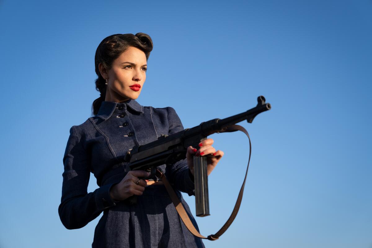 A woman with a submachine gun objects.