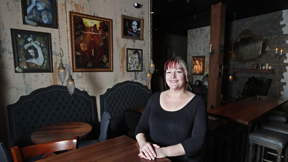 Owner Lara Hanneman poses near some of the artwork at her Cauldron Spirits and Brews bar and restaurant in Buena Park.