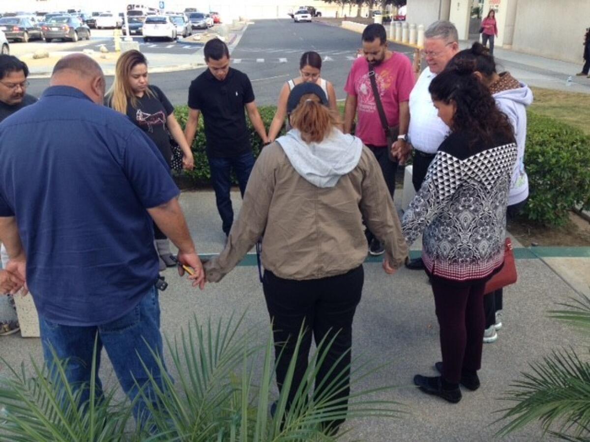 A group of people hold hands in prayer outside of the Arrowhead Regional Medical Center following a shooting at the Inland Regional Center in San Bernardino.