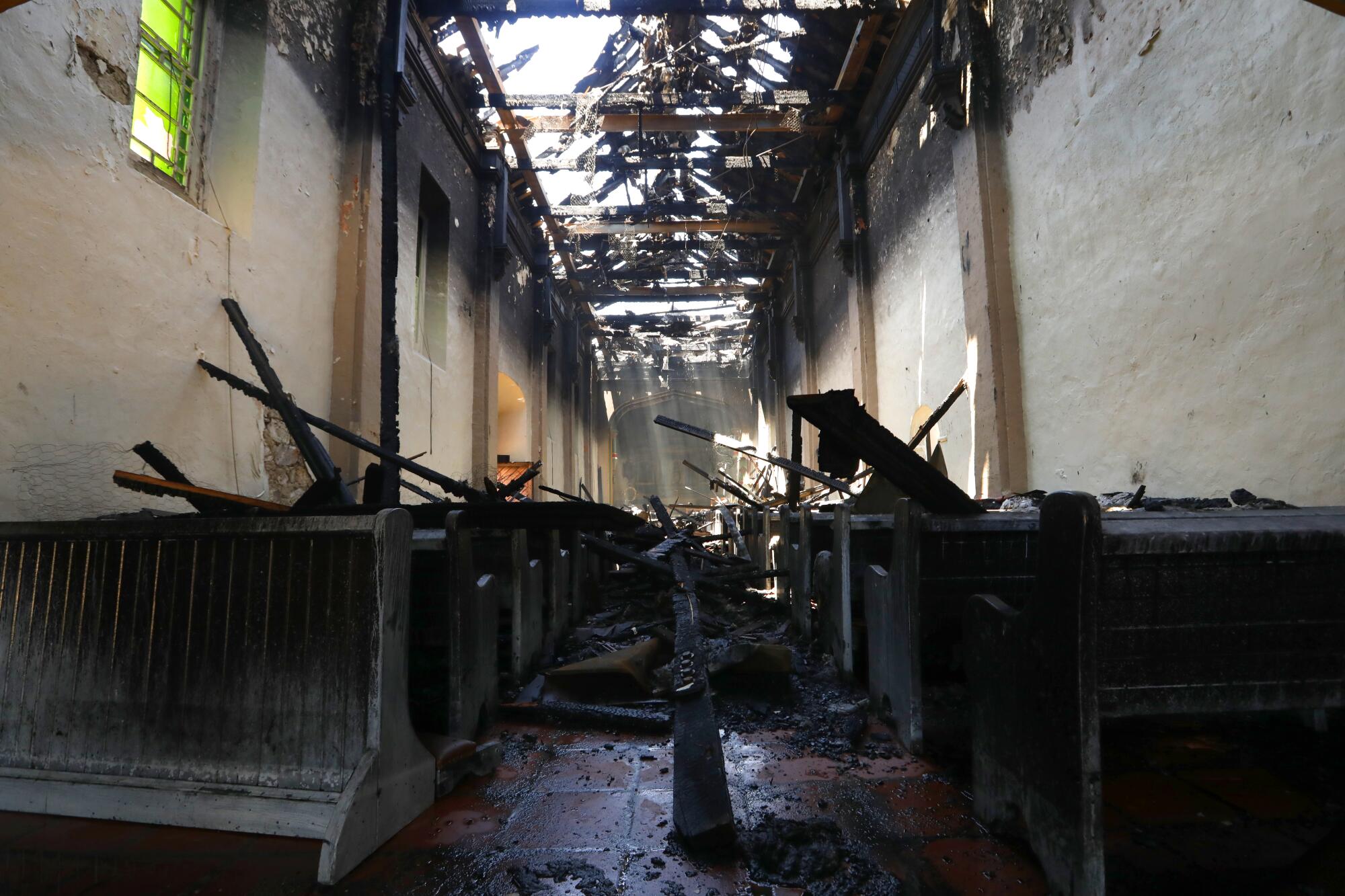 Sunlight beams through the destroyed roof onto charred pews inside the San Gabriel Mission