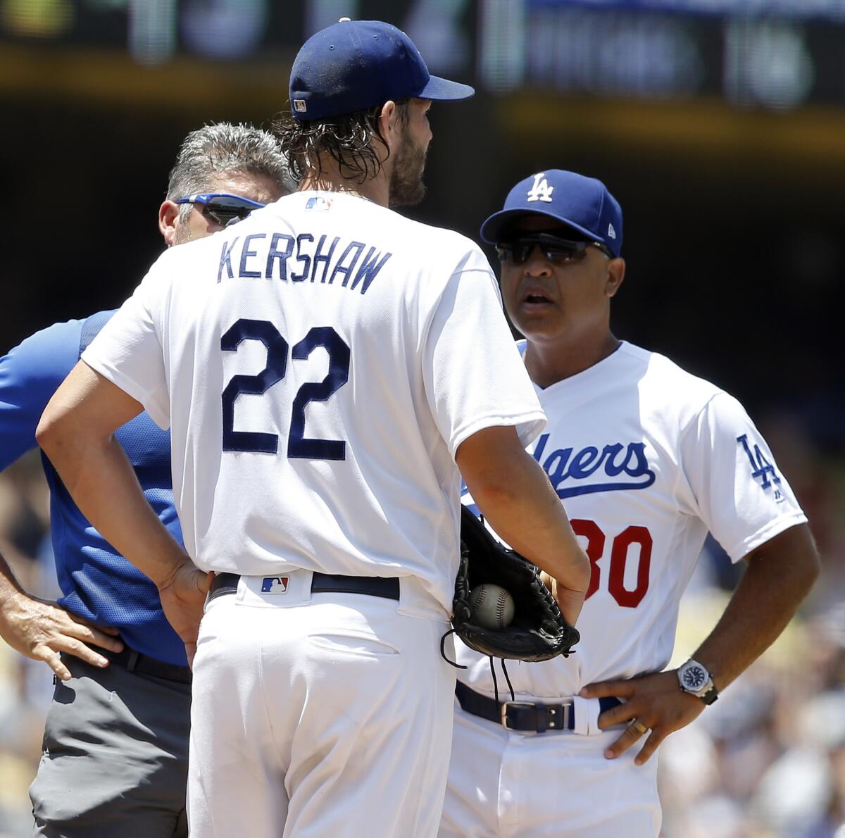 El abridor Clayton Kershaw, centro, de los Dodgers de Los Ángeles, dialoga con el manager Dave Roberts, derecha, y el entrenador Nathan Lucero en el segundo inning del partido ante los Bravos de Atlanta, en Los Ángeles, el domingo 23 de julio de 2017.