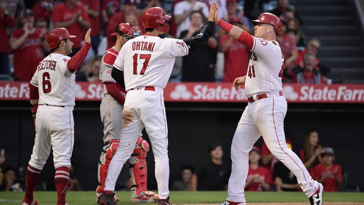 Angels' Justin Bour, right, is congratulated by Shohei Ohtani (17) and David Fletcher, left, as Cincinnati Reds catcher Curt Casali stands at the plate during the eighth inning on Wednesday at Angel Stadium.