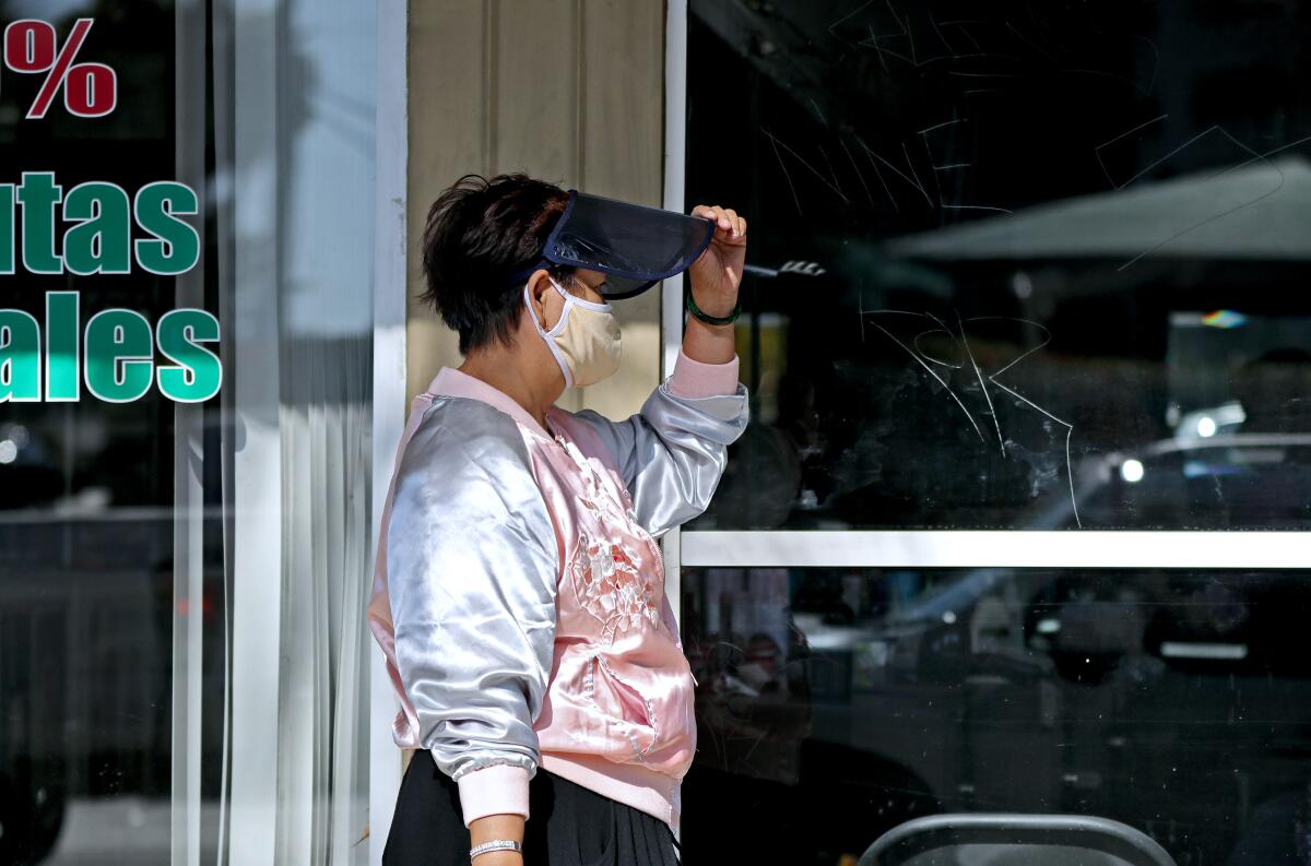 A woman wears a face mask and a face shield as she walks on the 600 block of West 19th Street in Costa Mesa on Saturday.