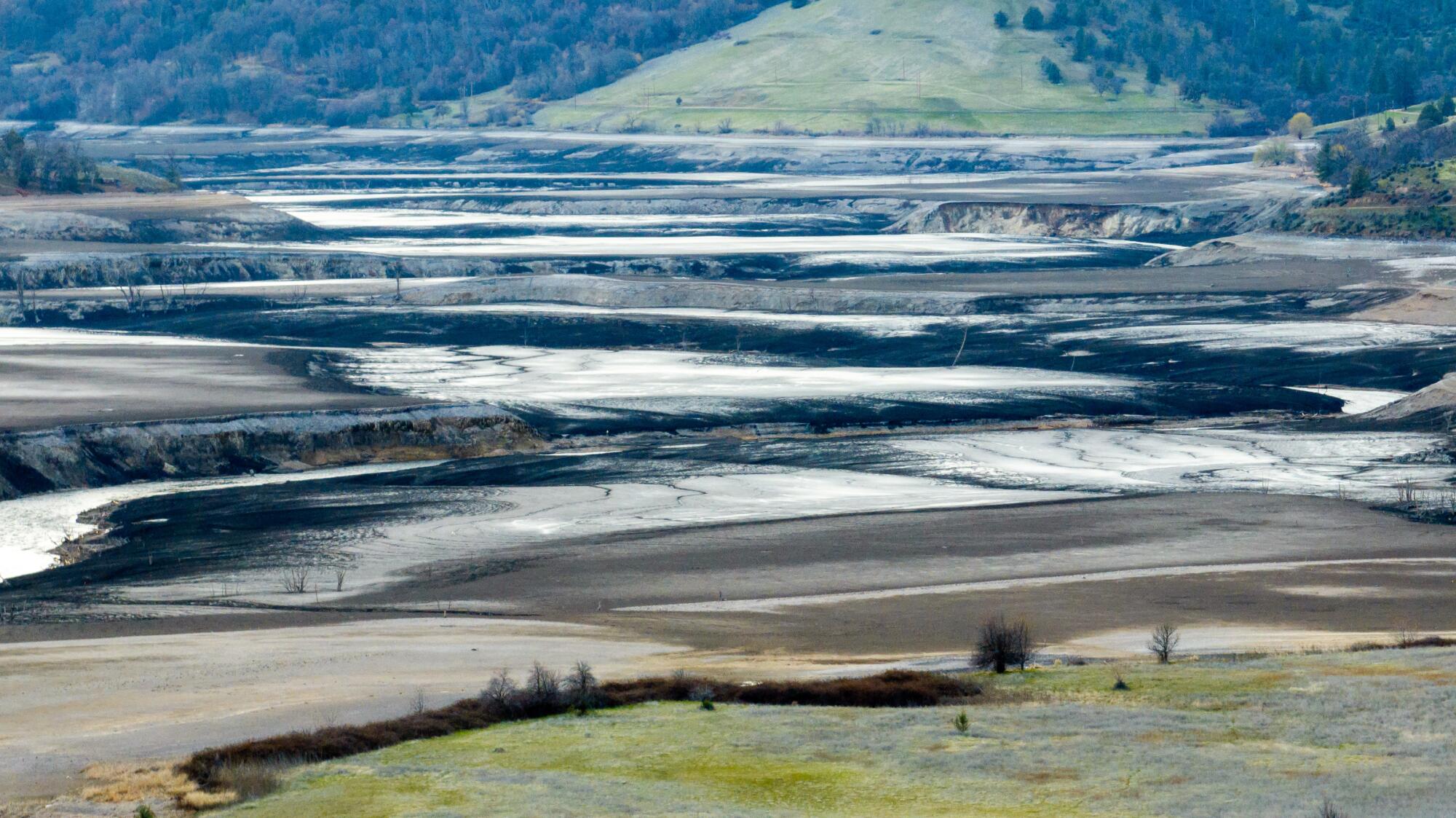 Water in a series of mudflats at decreasing elevations, from a hill in the background down to flat land in the foreground