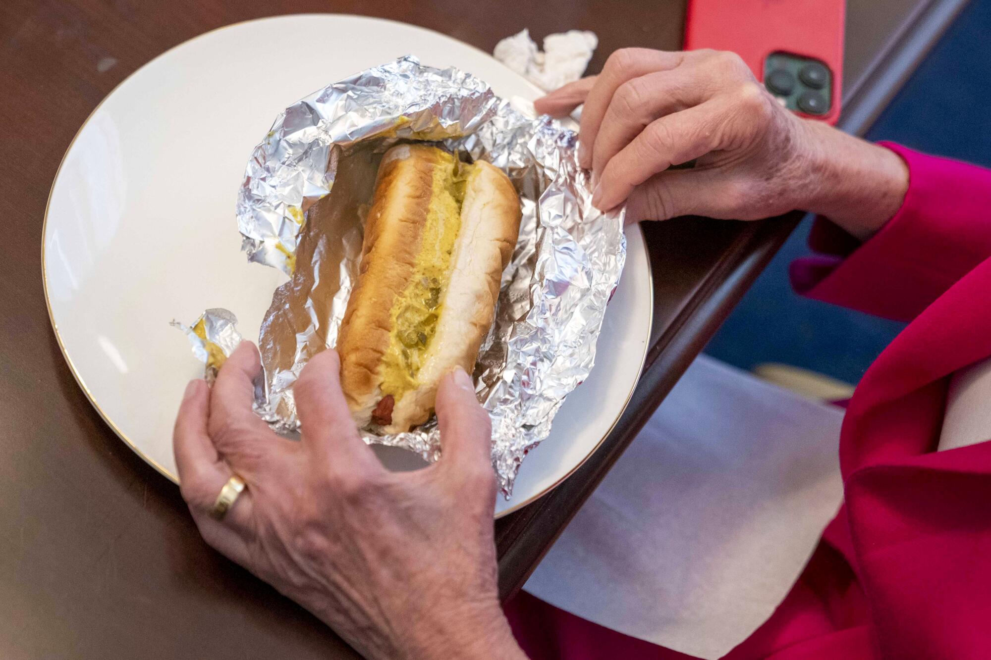 Nancy Pelosi opens a hot dog with mustard and relish for lunch in her hideaway.