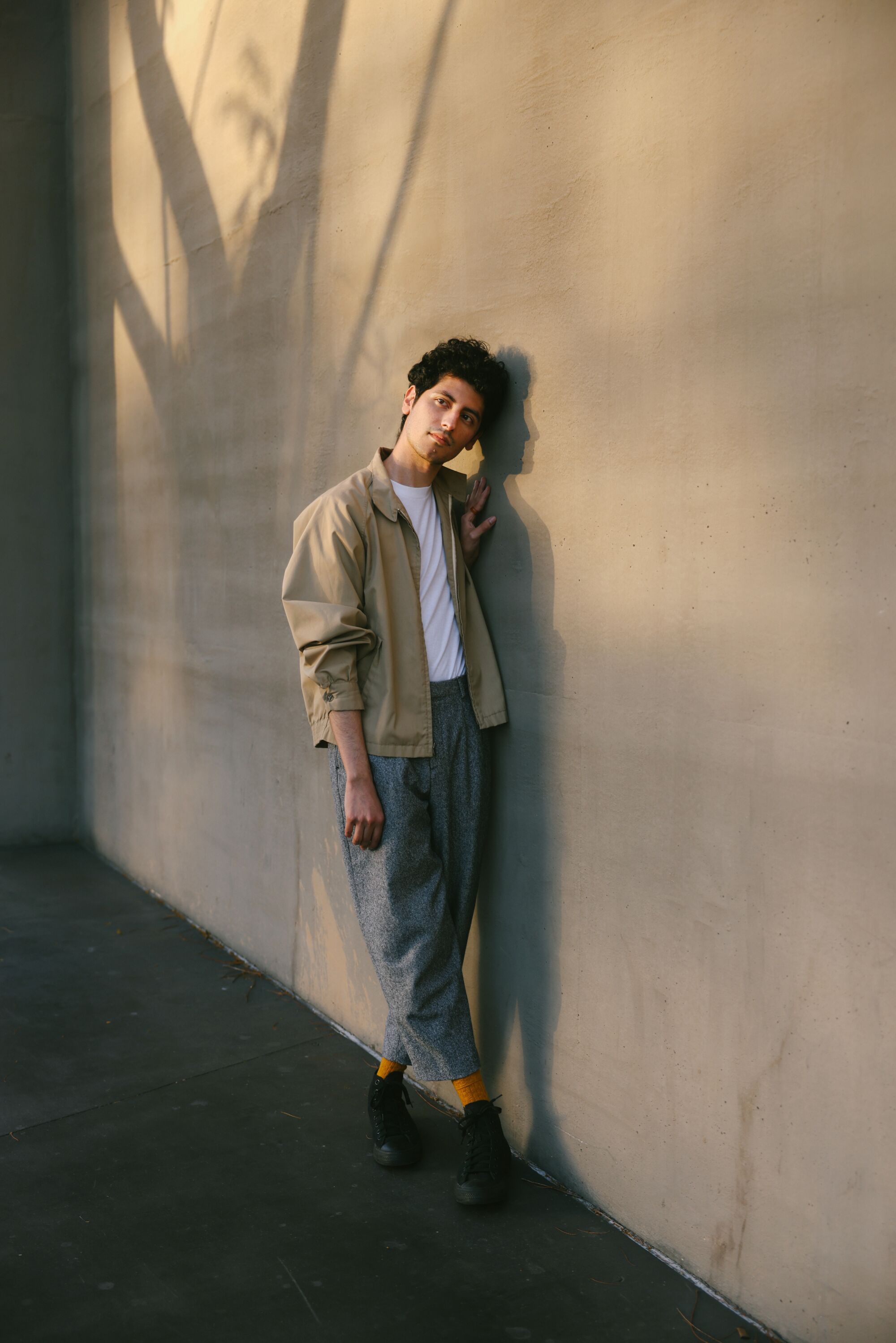 A man stands next to a white wall, leaning his head against it.