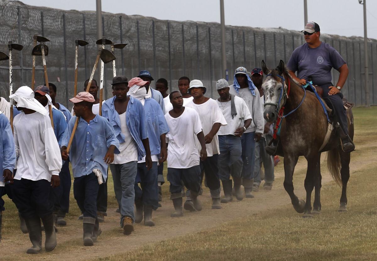 A prison guard rides a horse alongside men walking in line by a tall fence.