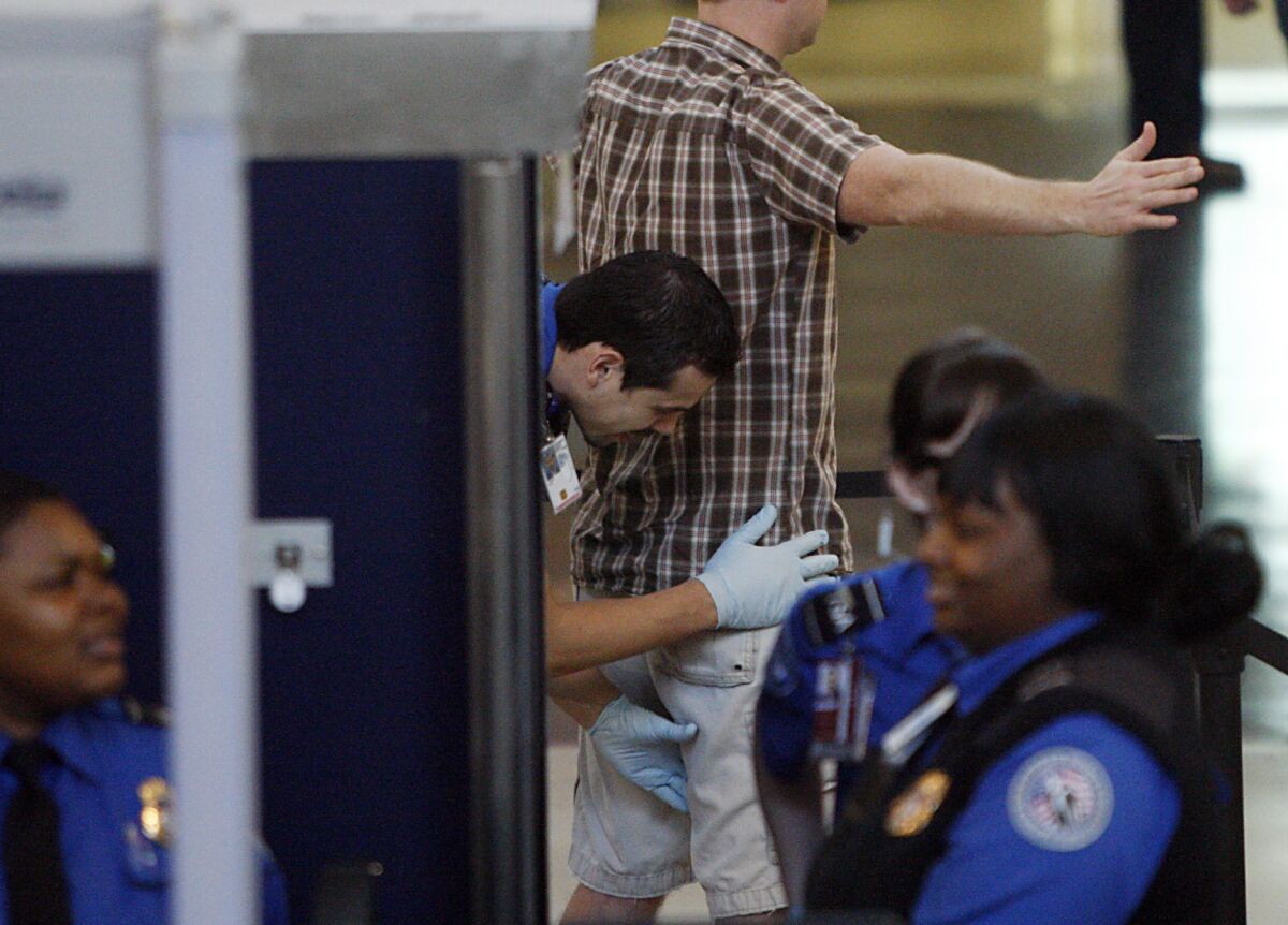 An airline passenger gets patted down by a TSA officer after passing through a metal detector.