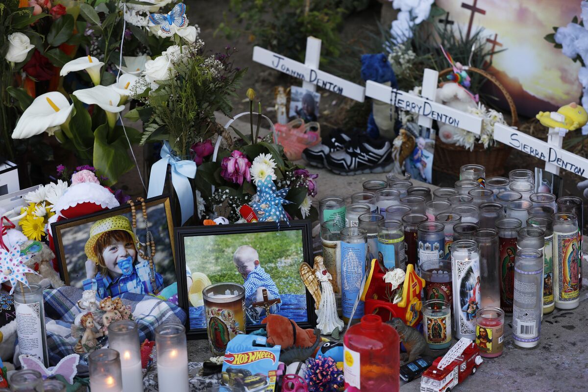 Photos, flowers, trinkets and candles in front of three small wooden crosses at a sidewalk memorial