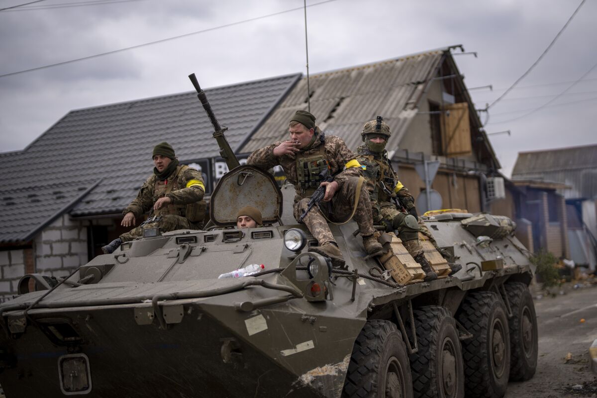 Soldiers with yellow armbands sit on a military vehicle