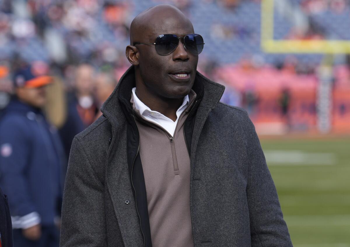 Terrell Davis wears sunglasses as he walks on the sideline before an NFL football game 