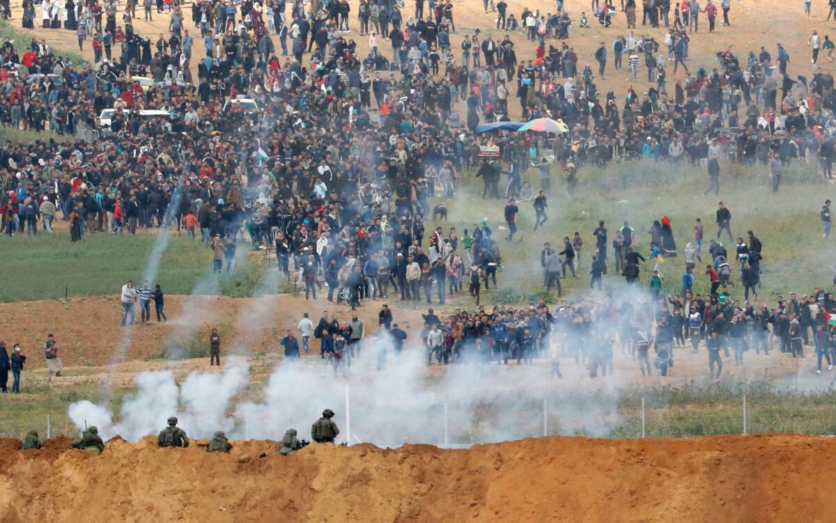 Tear gas grenades fall amid Palestinians gathered to protest along the Gaza Strip border with Israel on Land Day. Israeli soldiers hold positions in the foreground.
