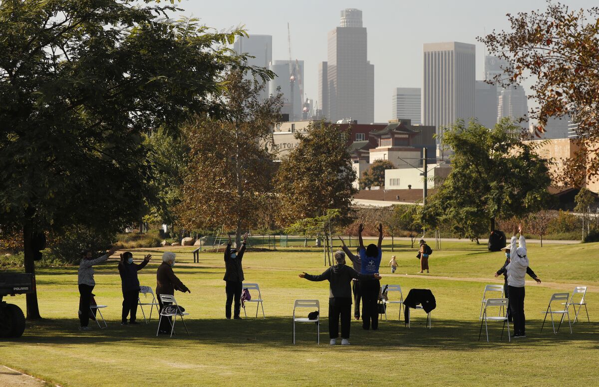 A group of people in masks spaced out in a circle in a park with downtown L.A.'s skyline in the background