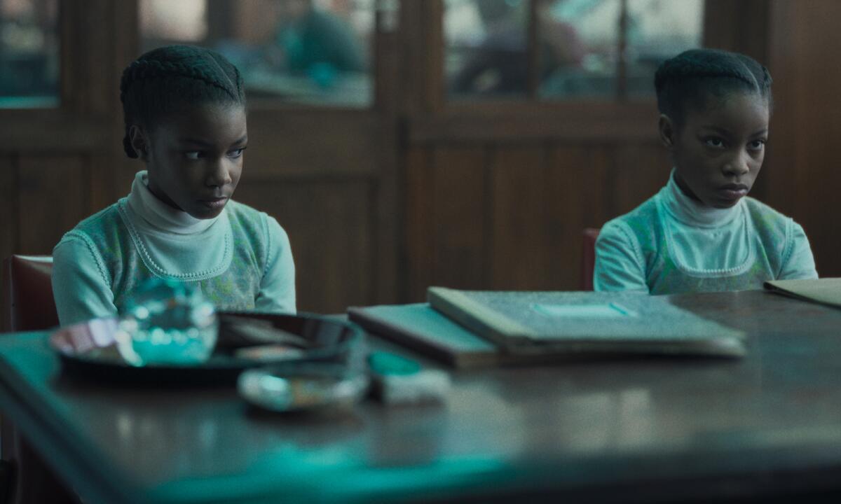 Two girls dressed identically sitting at a desk in the movie "The Silent Twins."