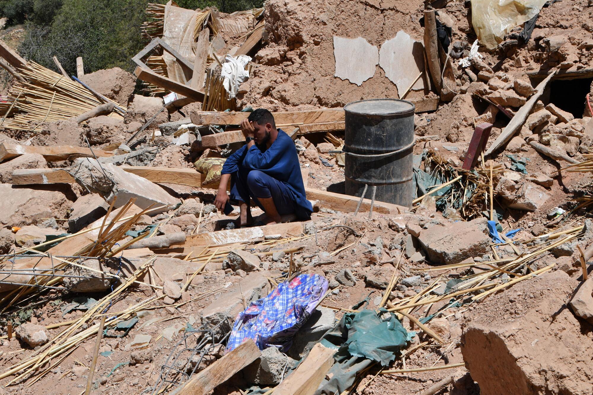 A man cries as he sits on the rubble of a house.