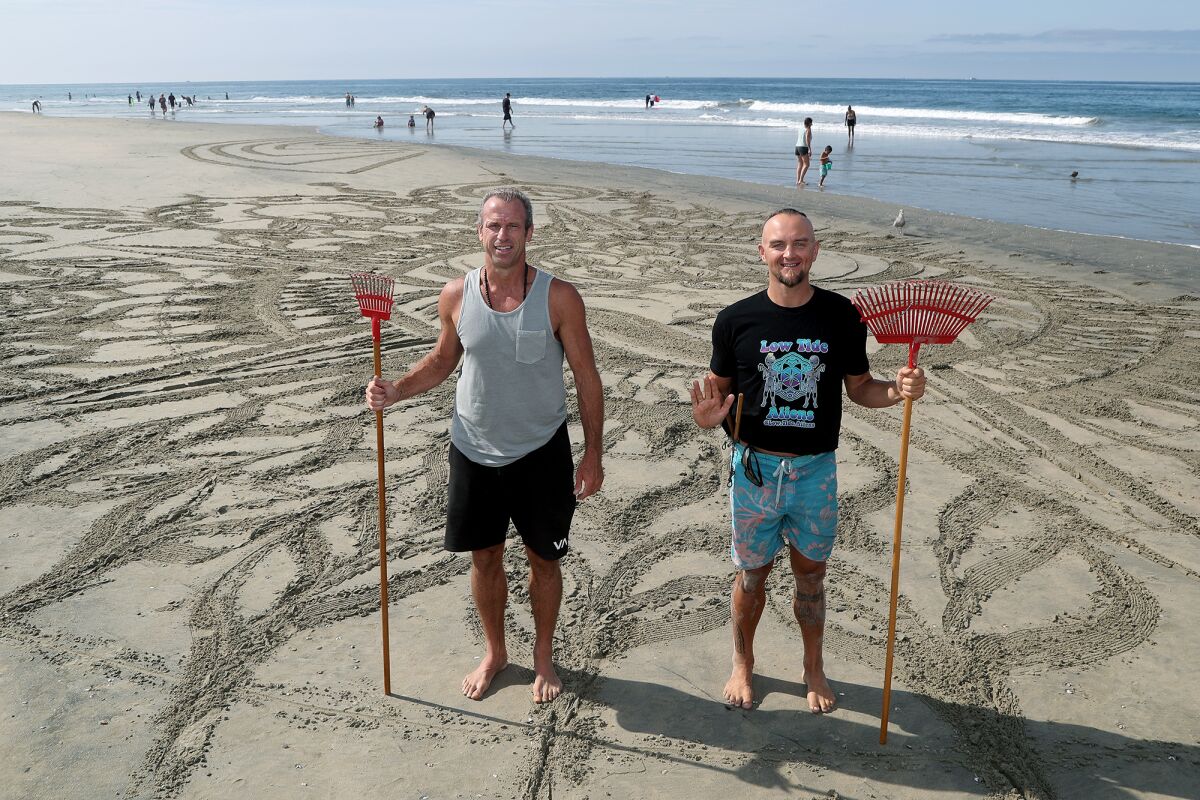 Shane Kern and Drew Davis pose with their rakes at a temporary Low Tide Aliens installation at Newport Beach Pier.