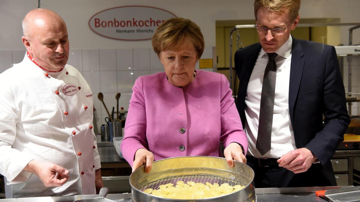 German Chancellor Angela Merkel is flanked by the Christian Democratic party's top candidate for the Schleswig-Holstein stage election, Daniel Guenther, right, and business owner Hermann Hinrichs while visiting a candy shop in Eckernfoerde, northern Germany, on May 5, 2017.
