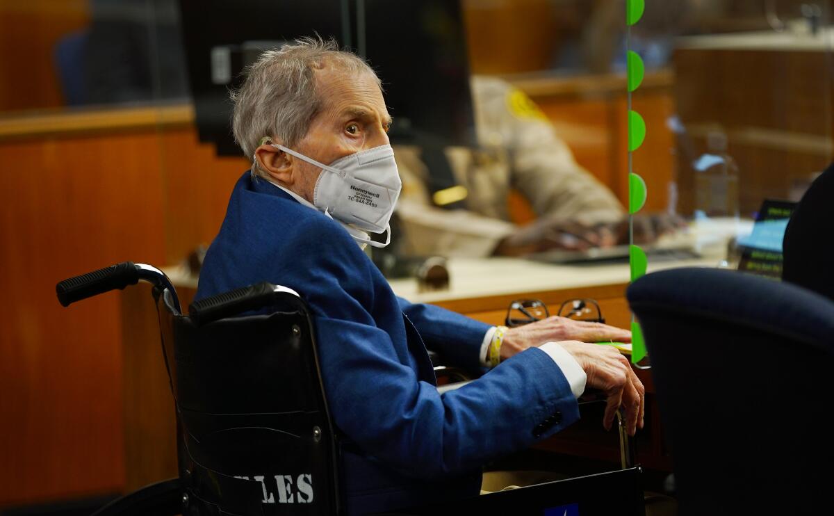 Robert Durst, wearing a mask, sits in a wheelchair in court.