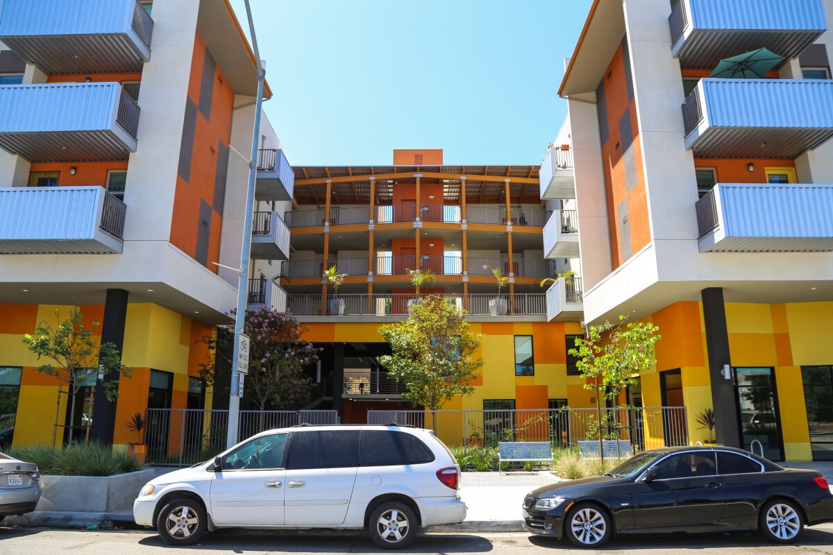 The mid-rise affordable-housing development Encanto Village as seen from the street, with cars parked in front.