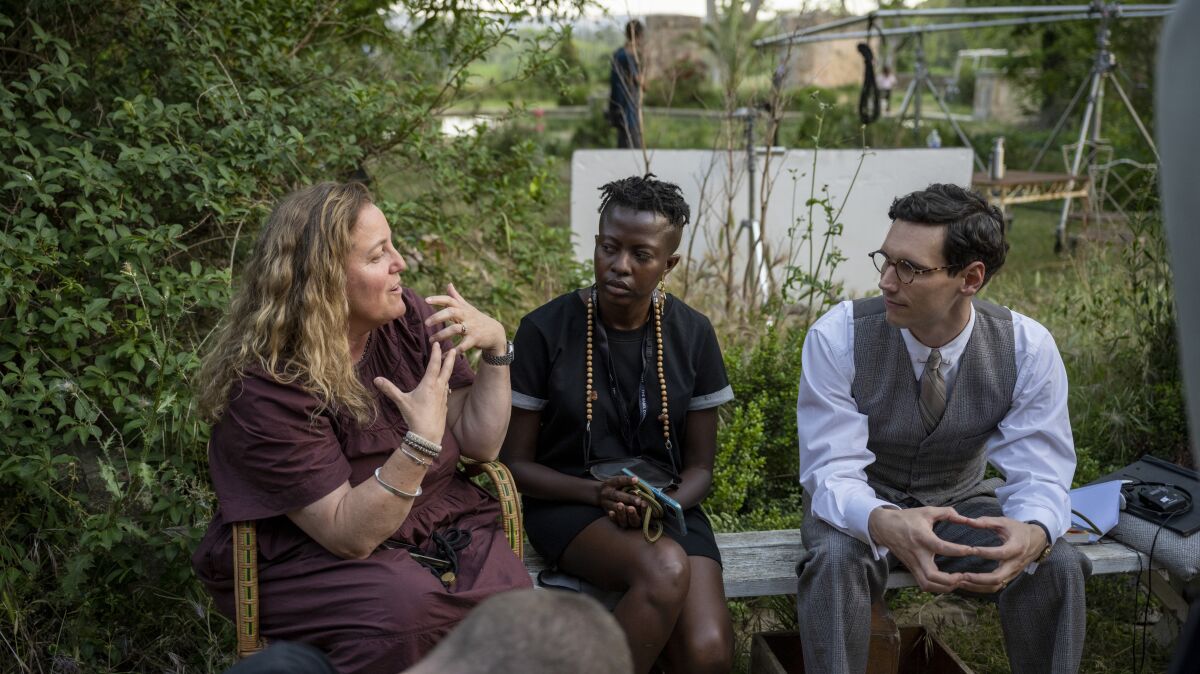 A woman speaks to another woman and a man in period costume behind the scenes of a TV show