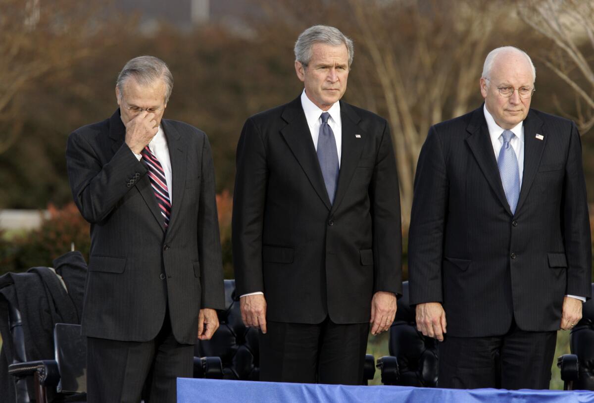 En esta fotografía de archivo del viernes 15 de diciembre de 2006, el secretario de Defensa Donald Rumsfeld, izquierda, se toca la nariz con la mano mientras el presidente George W. Bush y el vicepresidente Dick Cheney participan en la ceremonia.