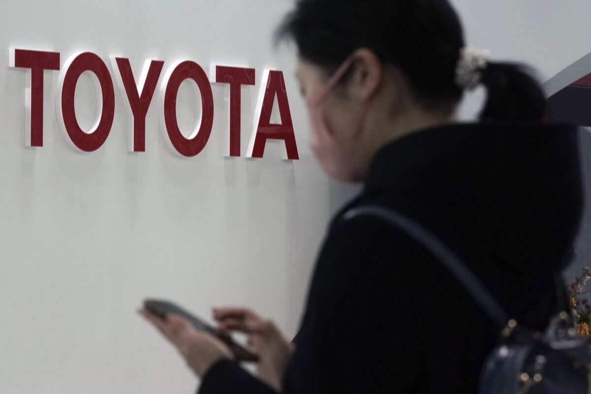 FILE - In this Jan. 30, 2020, file photo, a visitor stands by the logo of Toyota Motor Corp. at its showroom in Tokyo. Toyota’s April-June profit plunged 74% as the coronavirus pandemic crushed vehicle sales to about half of what the top Japanese automaker sold the previous year, reported Thursday, Aug. 6, 2020. (AP Photo/Eugene Hoshiko, File)