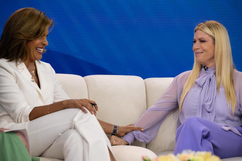 Hoda Kotb, left, and Jill Martin hold hands while sitting on a couch during the "Today" show.