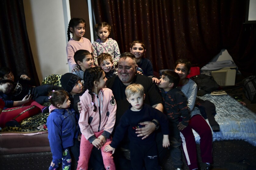 Edgar Kovacs pastor of the local Free Christian Church is surrounded by Roma children fleeing from Ukraine, inside a room of a Church in Didova Hora, Hungary, Friday, March 4, 2022. Edgar Kovacs, who leads the Free Christian Church in the Hungarian village of Uszka, offered up the only room in his church to house the entire family, which had fled from the western Ukrainian village of Didova Hora. (AP Photo/Anna Szilagyi)