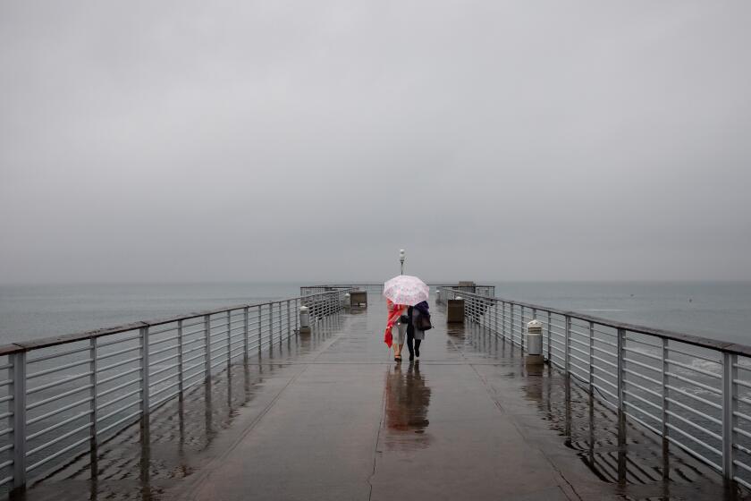 Hermosa Beach, CA - January 03: Two women share an umbrella while walking along the Hermosa Beach Pier in Hermosa Beach, CA, as rain fell across Los Angeles County, Tuesday, Jan. 3, 2023. (Jay L. Clendenin / Los Angeles Times)