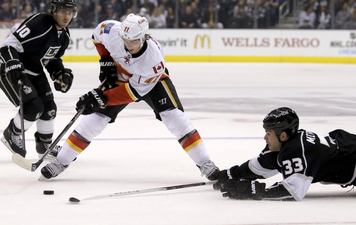 Kings defenseman Willie Mitchell, right, knocks the puck away from Calgary center Mikael Backlund as Mike Richards looks on Monday night.