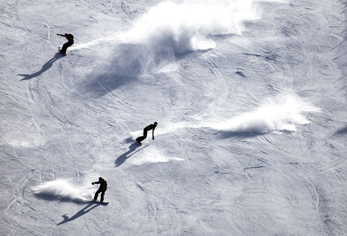 Snowboarders appear to surf on the snow on a steep run at Mammoth Mountain.