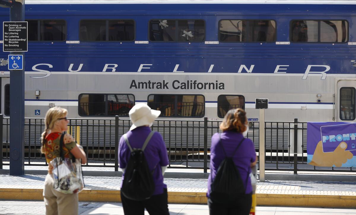 People stand near parked Amtrak Pacific Surfliner trains.