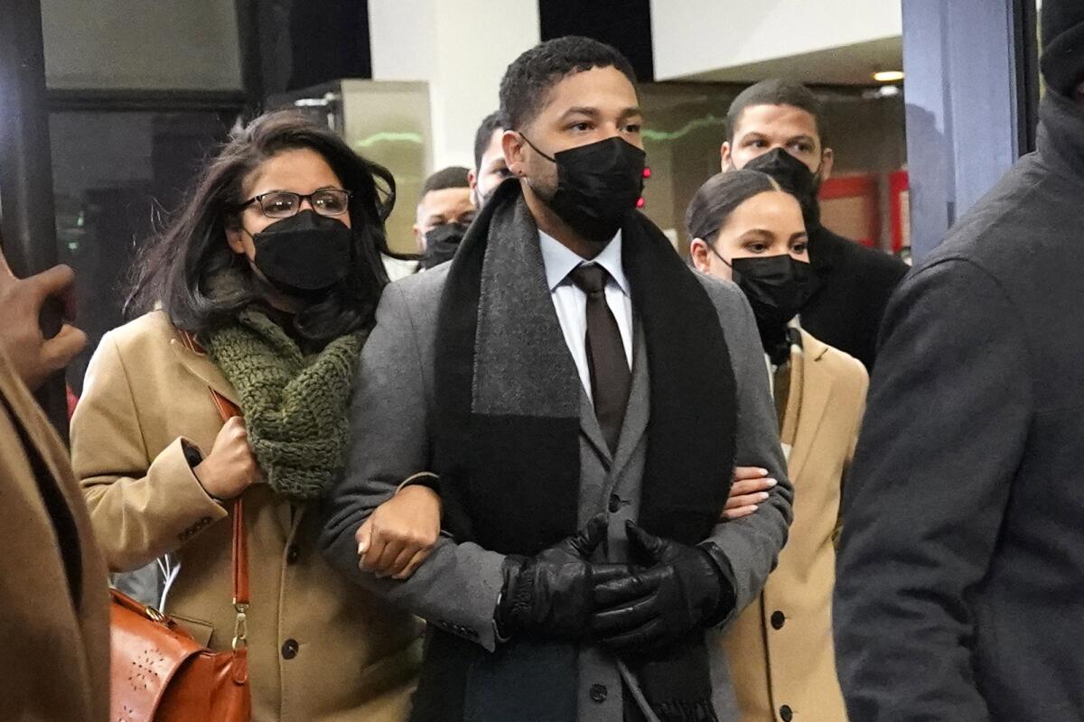 Jussie Smollett walks in a mask and coat, flanked by family members holding his arms.