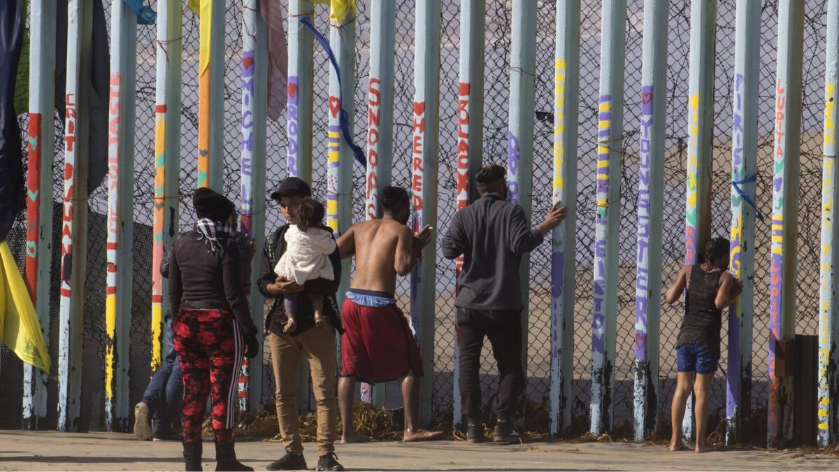 At center, a 22-year-old Honduran man says final words to his wife before he squeezed through the pillars in Tijuana on Wednesday carrying his young child.