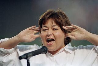 Comedienne Roseanne Barr holds her fingers in her ears as she screams the National Anthem between games of the San Diego Padres and the Cincinnati Reds doubleheader on July 25, 1990 in San Diego, Calif. She was booed loudly and she made an obscene gesture and spat when she was finished.