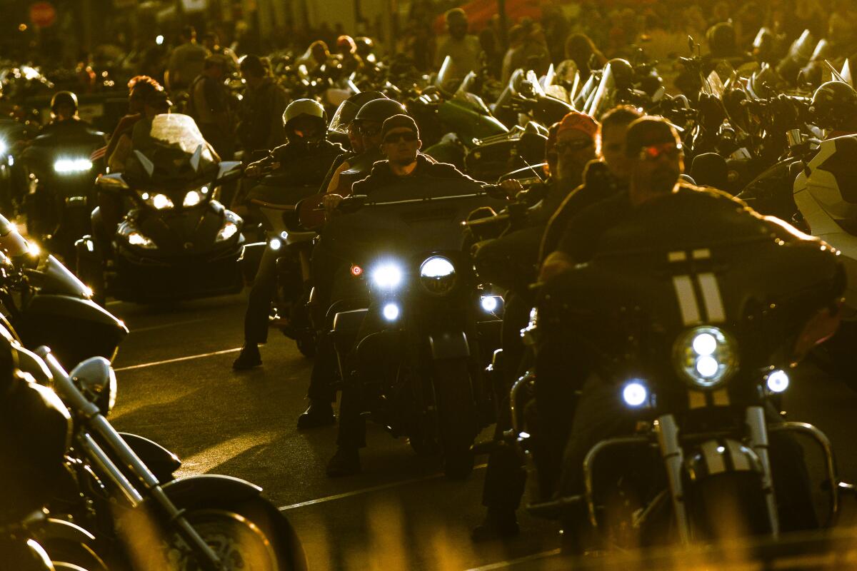 A line of motorcyclists ride between rows of other motorcycles