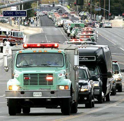 A U.S. Forest Service fire rig carrying the ashes of fallen firefighter Jason McKay leads a long procession of fire protection agency trucks along Hook Blvd. Next of kin follow in the two black vehicles after the funeral at High Desert Church.