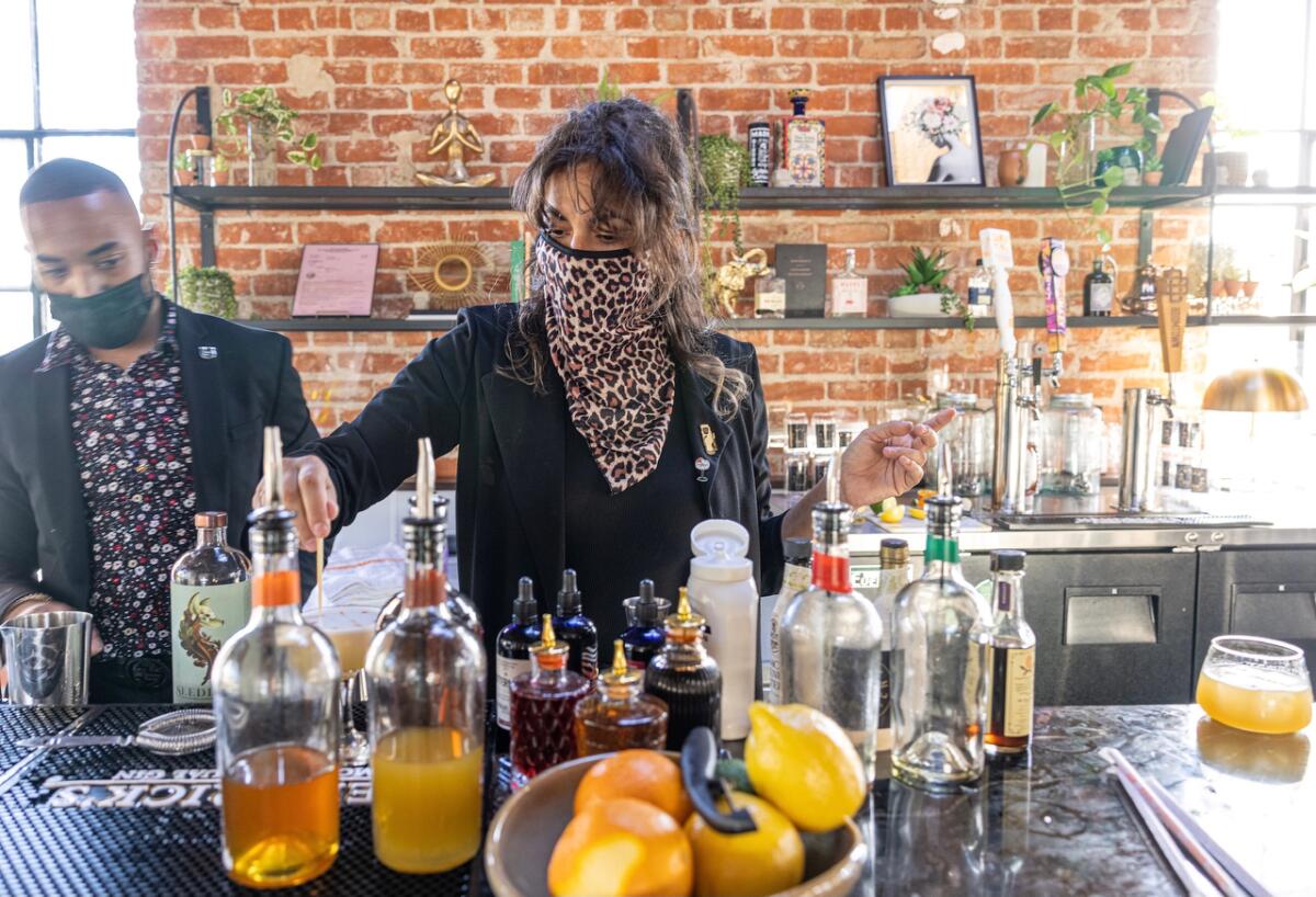 Masked people at a bar, which contains bottles of alcohol and bowls of fruit.